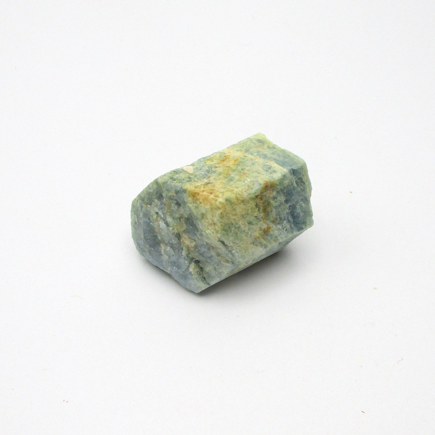 A rough Aquamarine crystal with a translucent blue and yellow coloring on a white background.