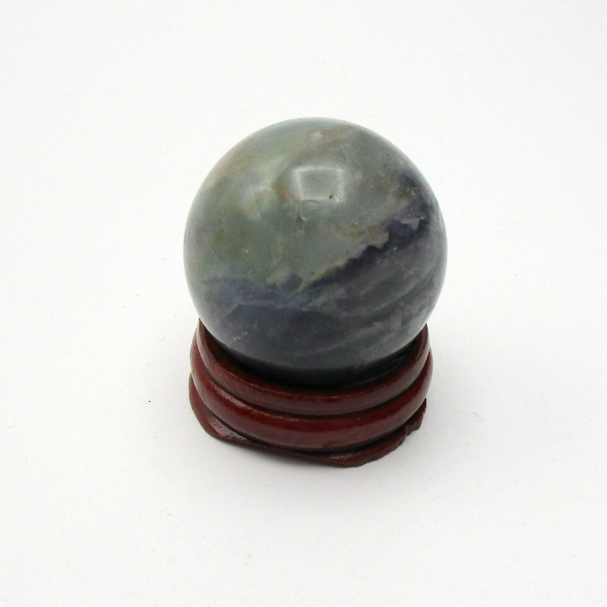 A polished fluorite sphere with a dark rich color, placed on a red wooden stand.