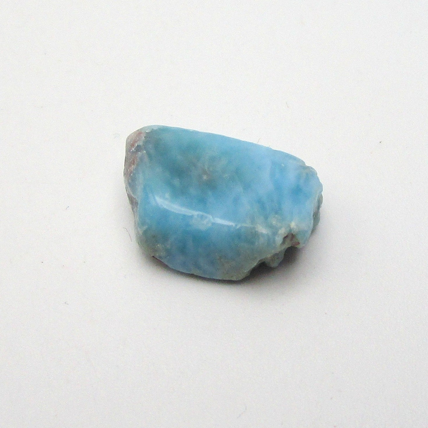 A polished piece of blue Larimar crystal on a white background