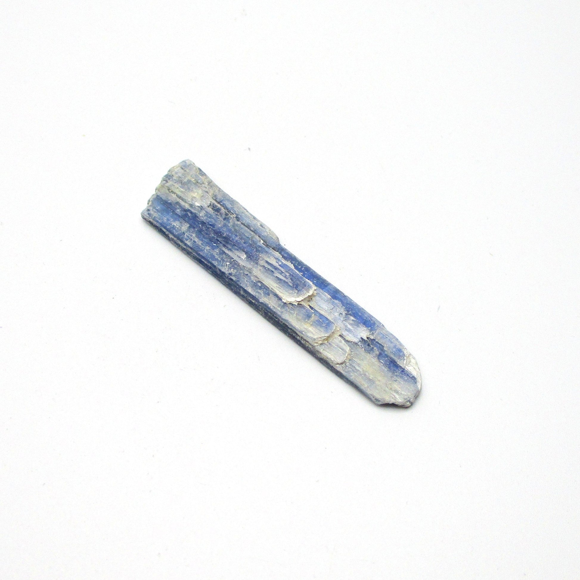 A rough, unpolished piece of blue kyanite crystal with natural imperfections on a white background