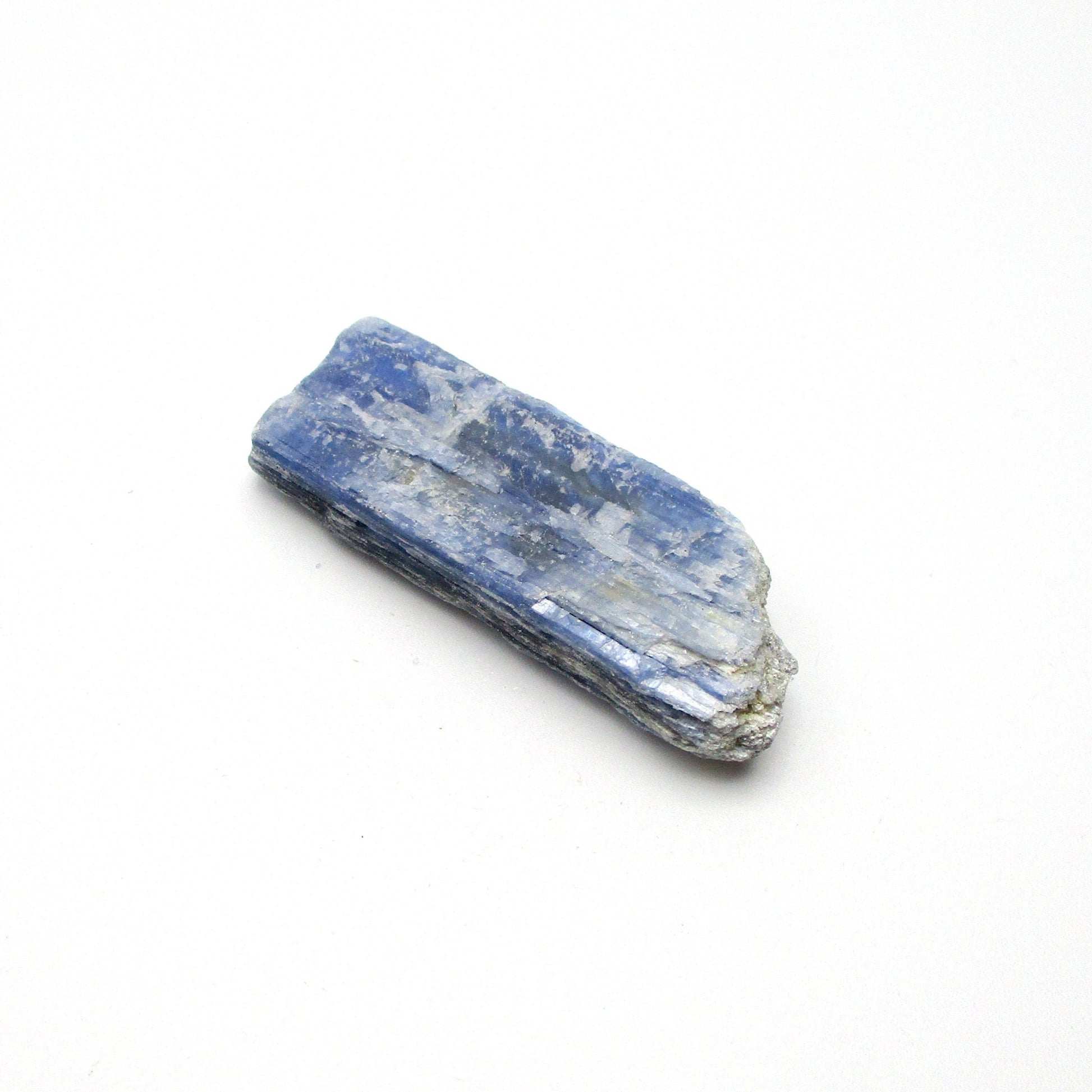 A rough, unpolished piece of blue kyanite crystal with natural imperfections on a white background