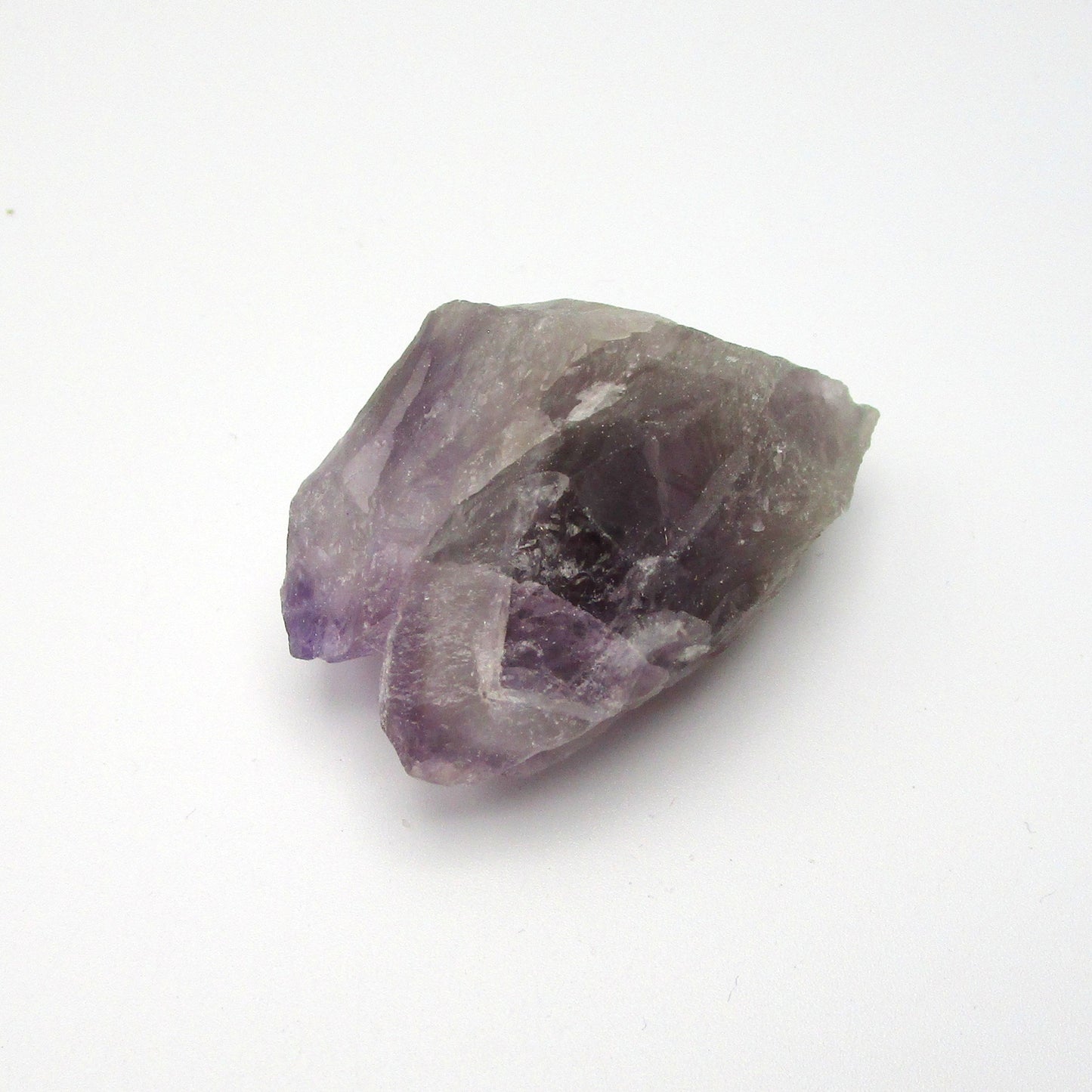 A rough Amethyst crystal with a range of purple colors against a white background.