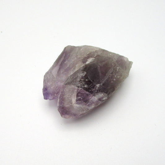 A rough Amethyst crystal with a range of purple colors against a white background.