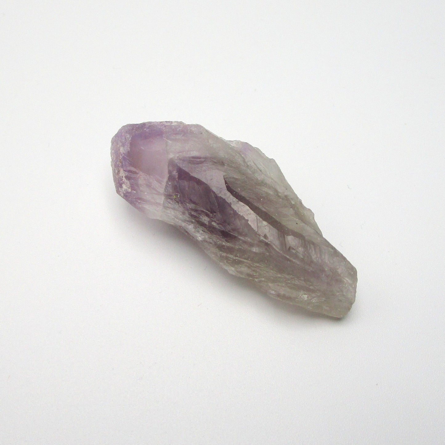 A Brazilian Amethyst Point crystal with a range of purple colors against a white background.
