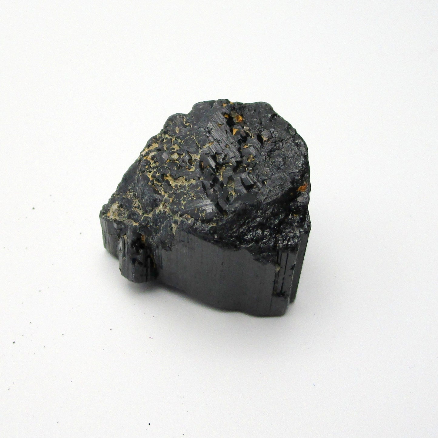 A rough, black crystal piece of Black Tourmaline against a white background.