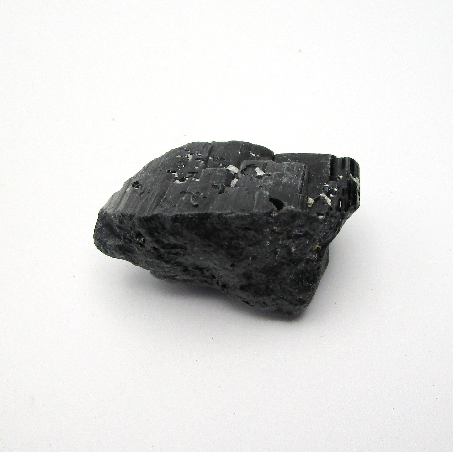 A rough, black tourmaline crystal with a metallic sheen, approximately 1 inch in size, displayed on a white background.
