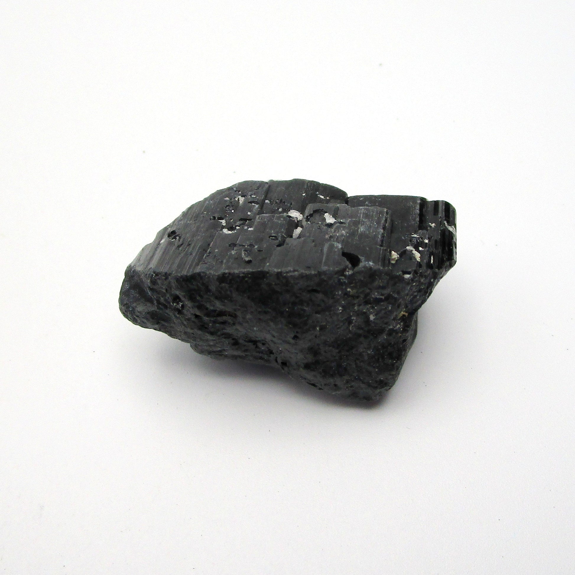 A rough, black tourmaline crystal with a metallic sheen, approximately 1 inch in size, displayed on a white background.
