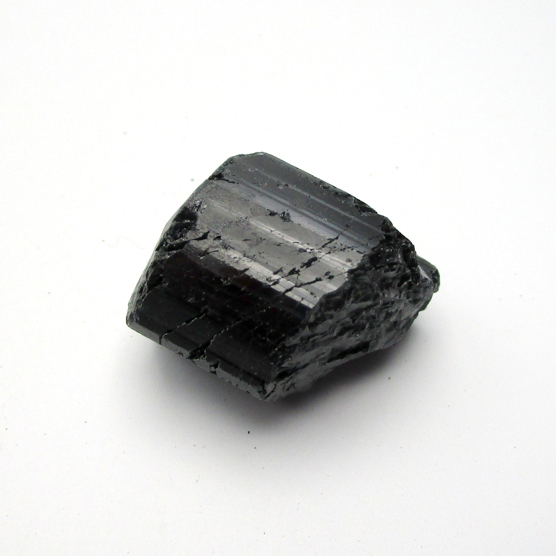 A rough, black tourmaline crystal with a metallic sheen, approximately 1 inch in size, displayed on a white background.