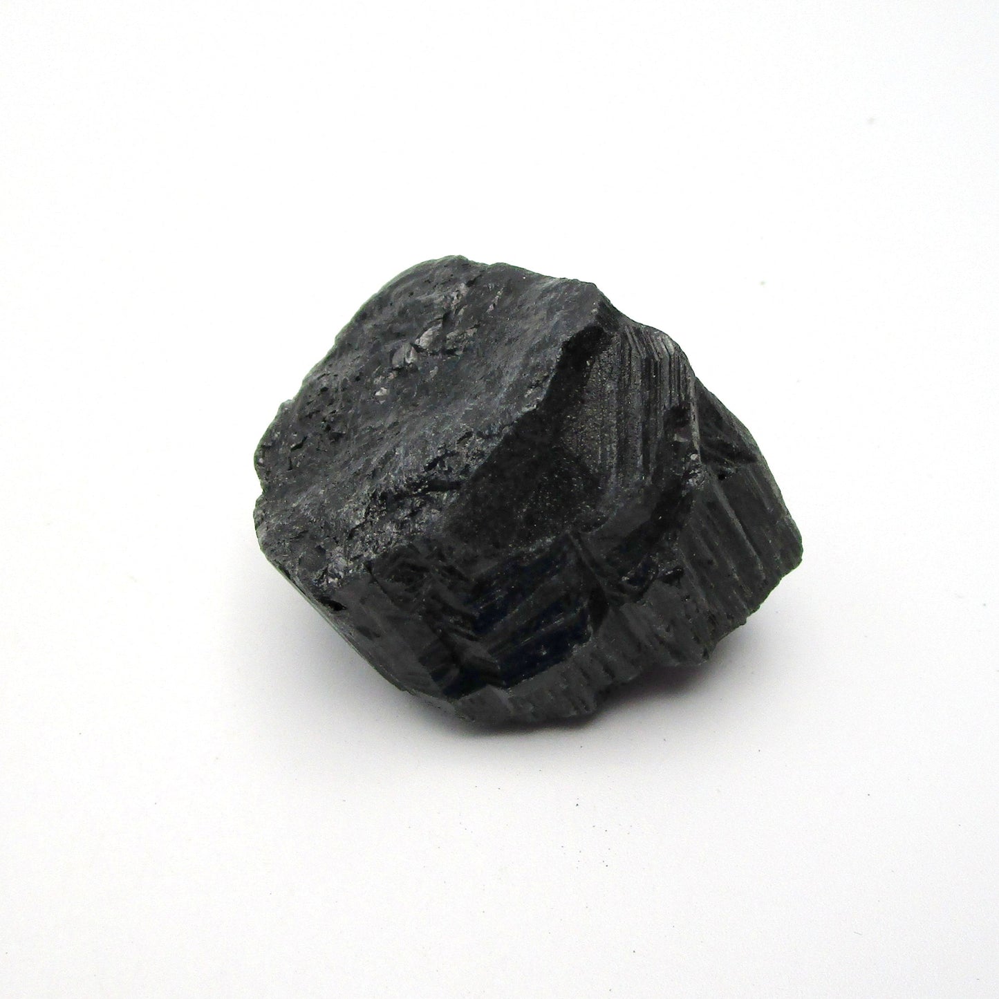 A rough, black tourmaline crystal with a metallic sheen, approximately 1 inch in size, displayed on a white background.