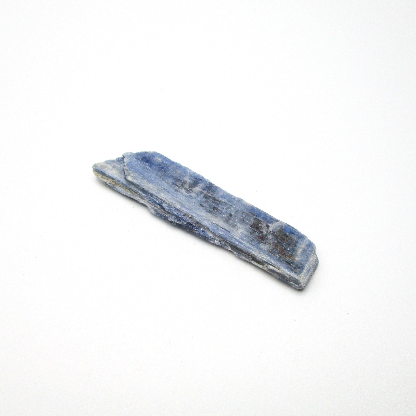 A rough, unpolished piece of blue kyanite crystal with natural imperfections on a white background