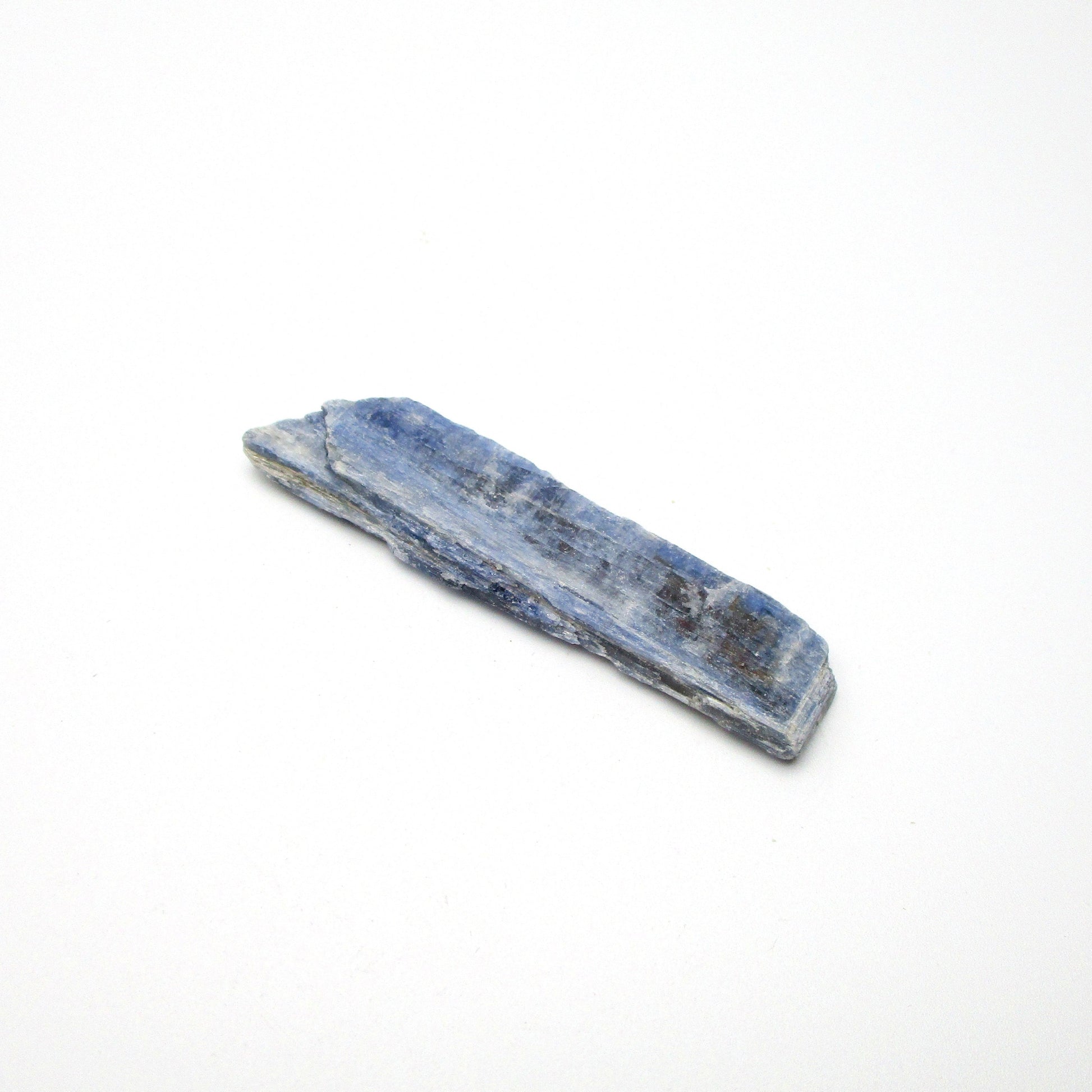 A rough, unpolished piece of blue kyanite crystal with natural imperfections on a white background