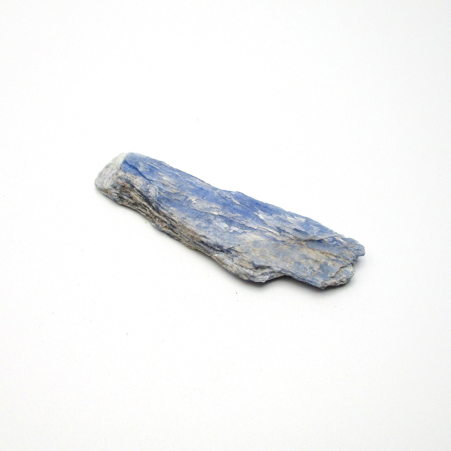 A rough, unpolished piece of blue kyanite crystal with natural imperfections on a white background