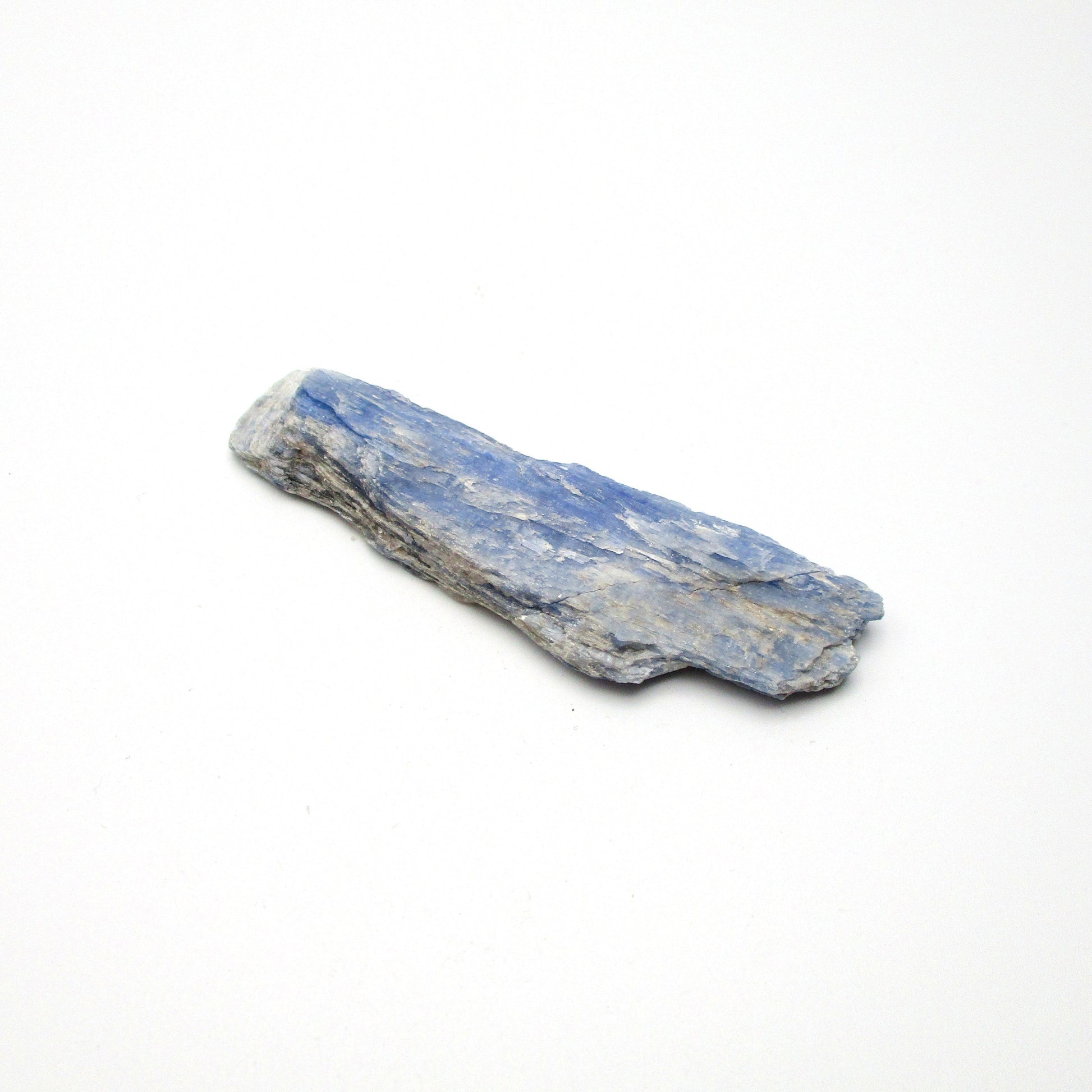 A rough, unpolished piece of blue kyanite crystal with natural imperfections on a white background