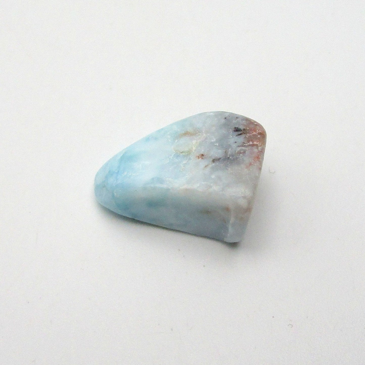 A polished, irregularly shaped piece of Larimar crystal with blue and white colors, placed on a white background.