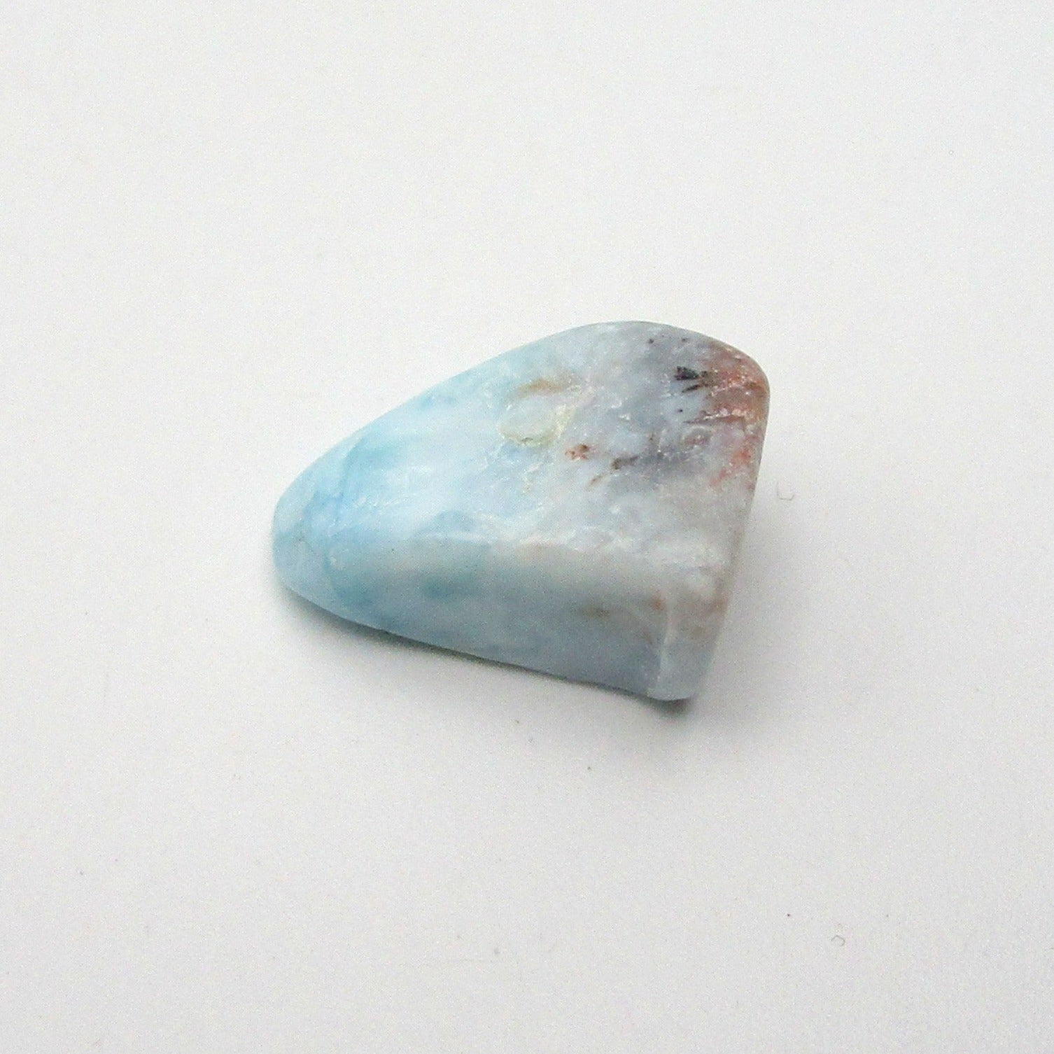 A polished, irregularly shaped piece of Larimar crystal with blue and white colors, placed on a white background.