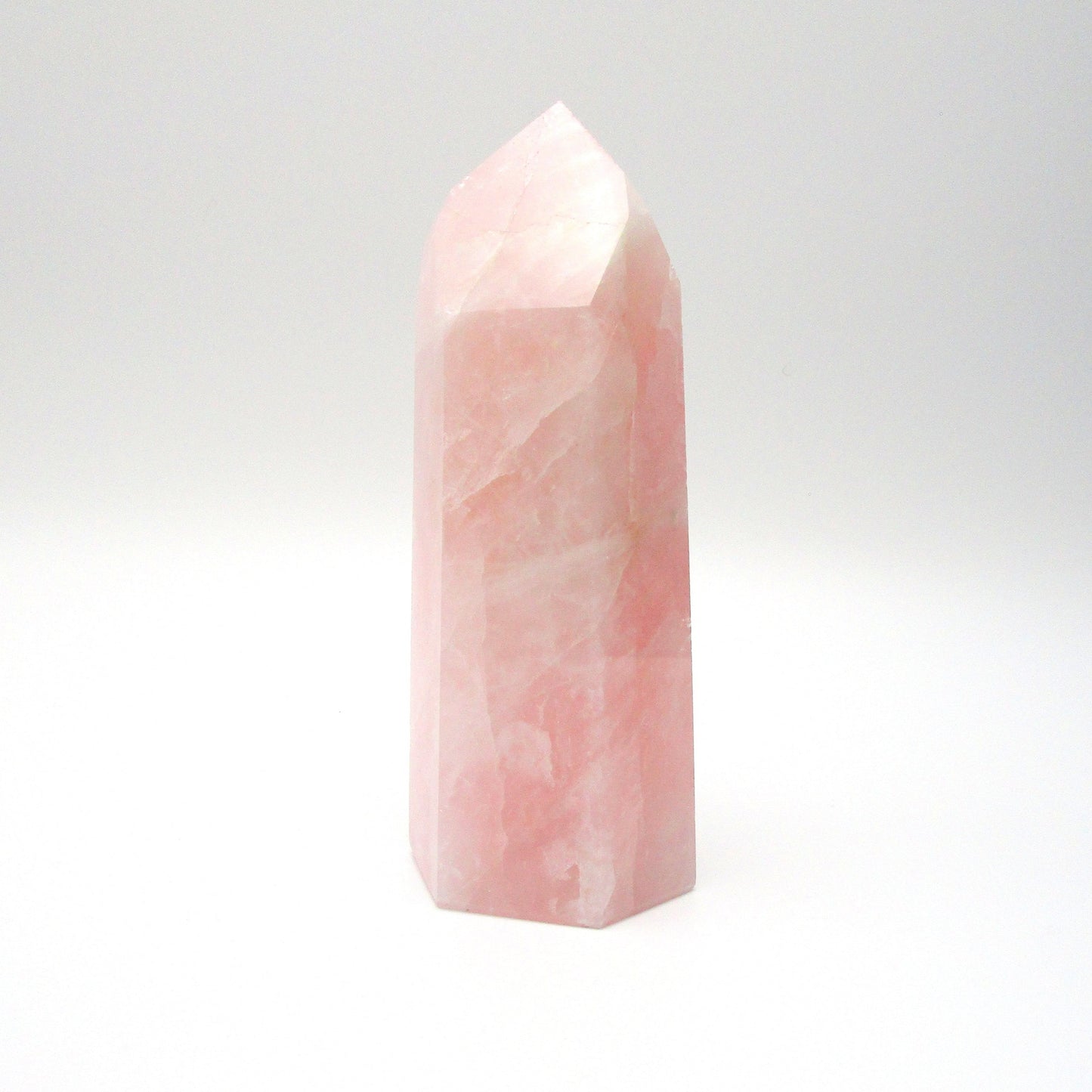 A polished pink rose quartz crystal in a tower shape, standing upright on a white background.
