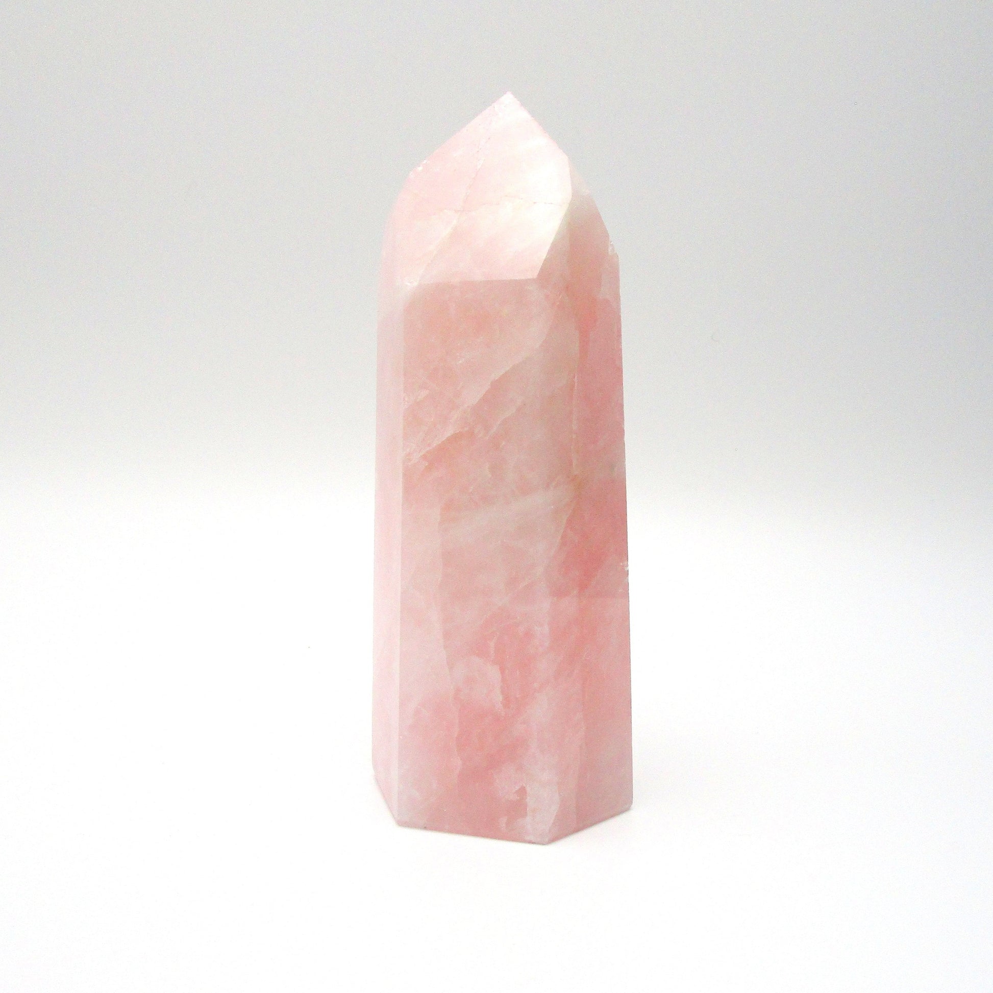 A polished pink rose quartz crystal in a tower shape, standing upright on a white background.